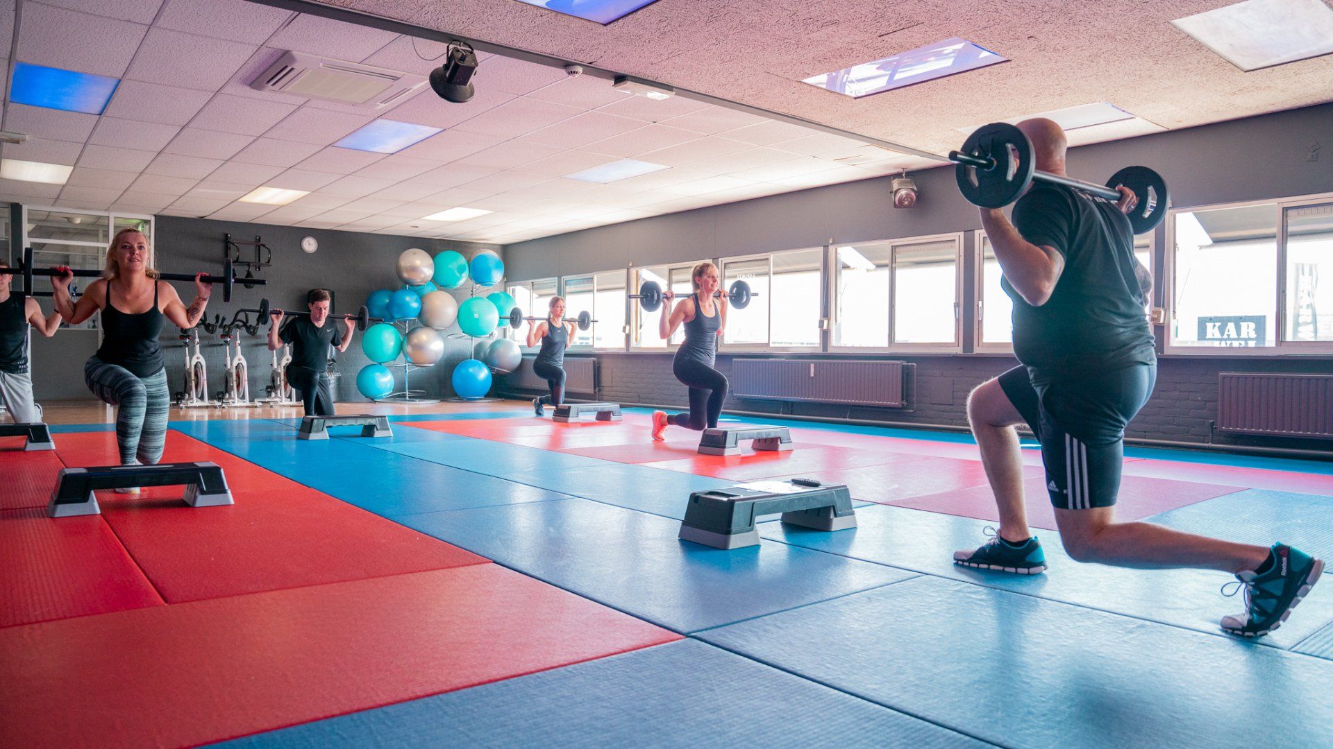 Een groep mensen doet yoga-oefeningen op een mat in een sportschool.