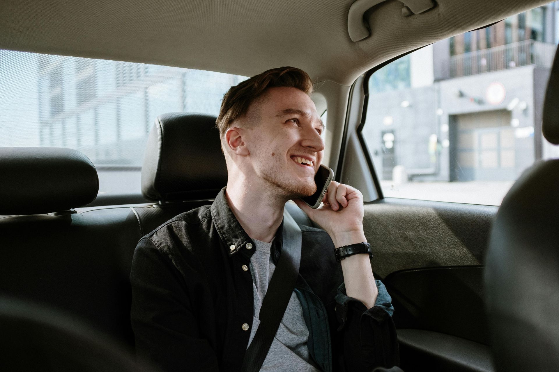 A man is sitting in the back seat of a car talking on a cell phone. Jado Mobile Auto Repair
