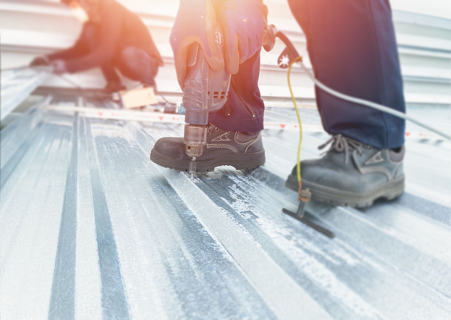 Roofing contractor fastening metal panels with a power drill during installation work. Roofing contractor fastening metal panels with a power drill during installation work.