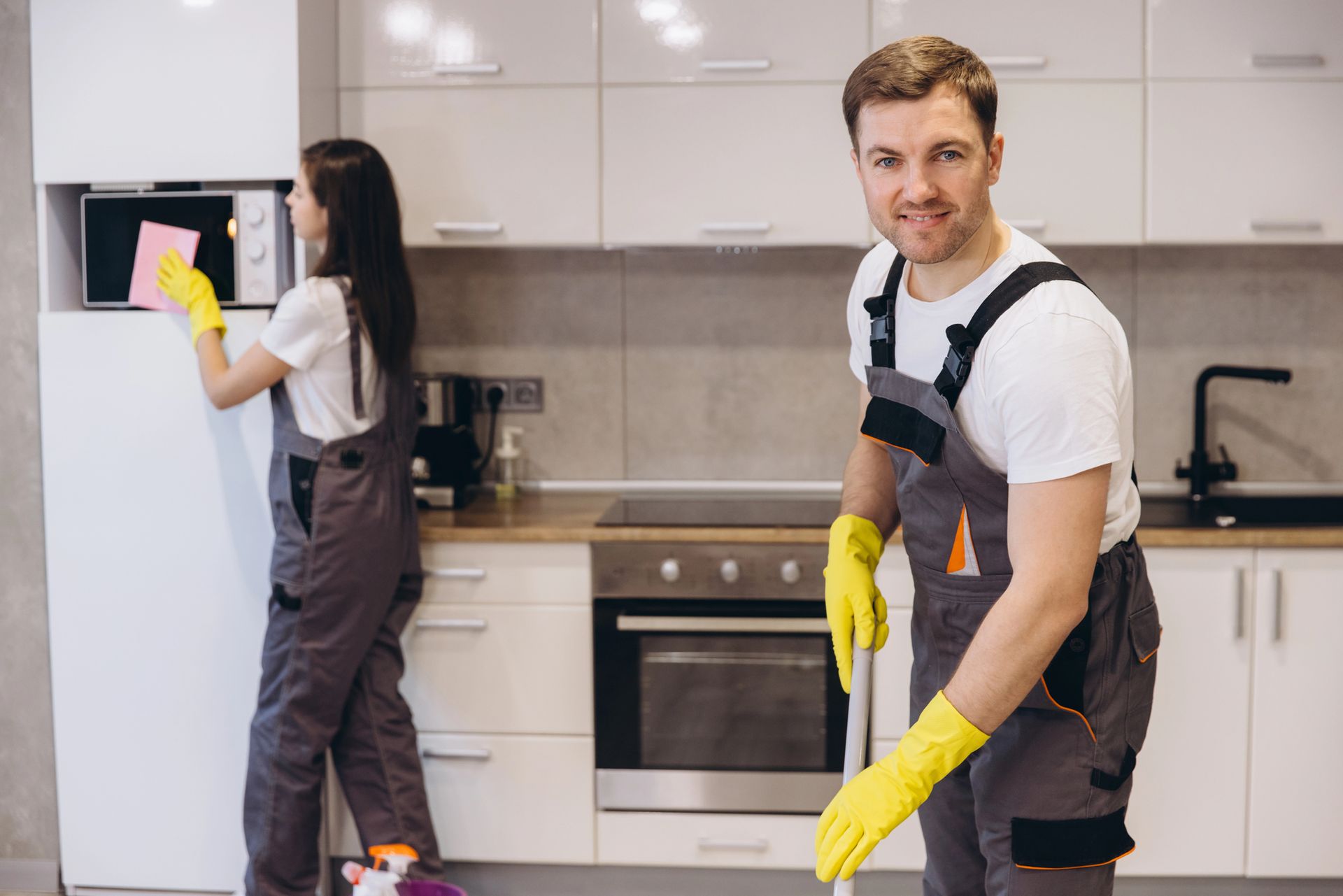 Due persone puliscono la cucina: una pulisce il microonde, l'altra sorride mentre passa il mocio.