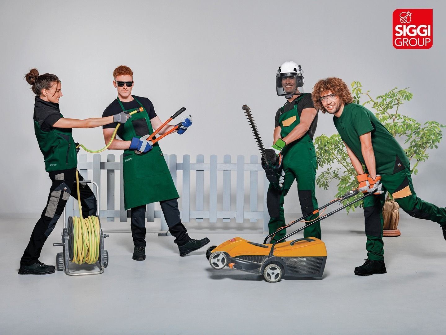 Quattro persone in abiti da lavoro verdi con attrezzi, tra cui un tosaerba e un tagliasiepi, vicino a una recinzione bianca, pubblicizzano il Siggi Group.