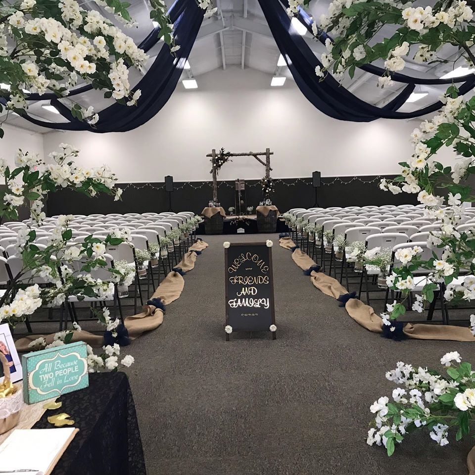 Decorated wedding ceremony aisle with white flowers, rows of chairs, and draped navy fabric ceiling.