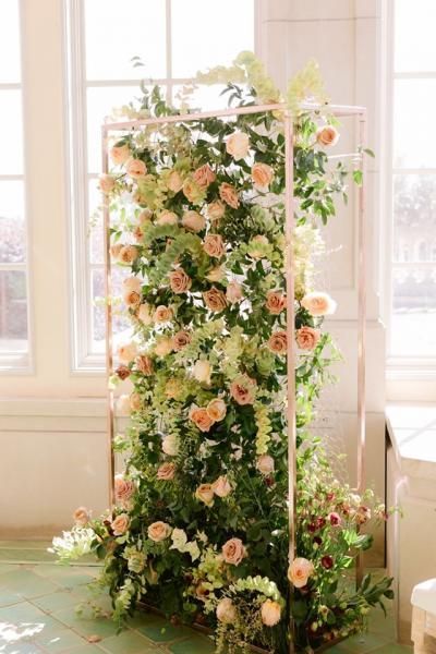 Tall floral arrangement of pale pink and white roses on a white metal frame by a bright window