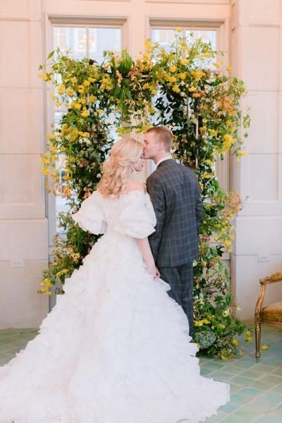 Bride and groom kissing beneath a floral arch at an outdoor wedding venue