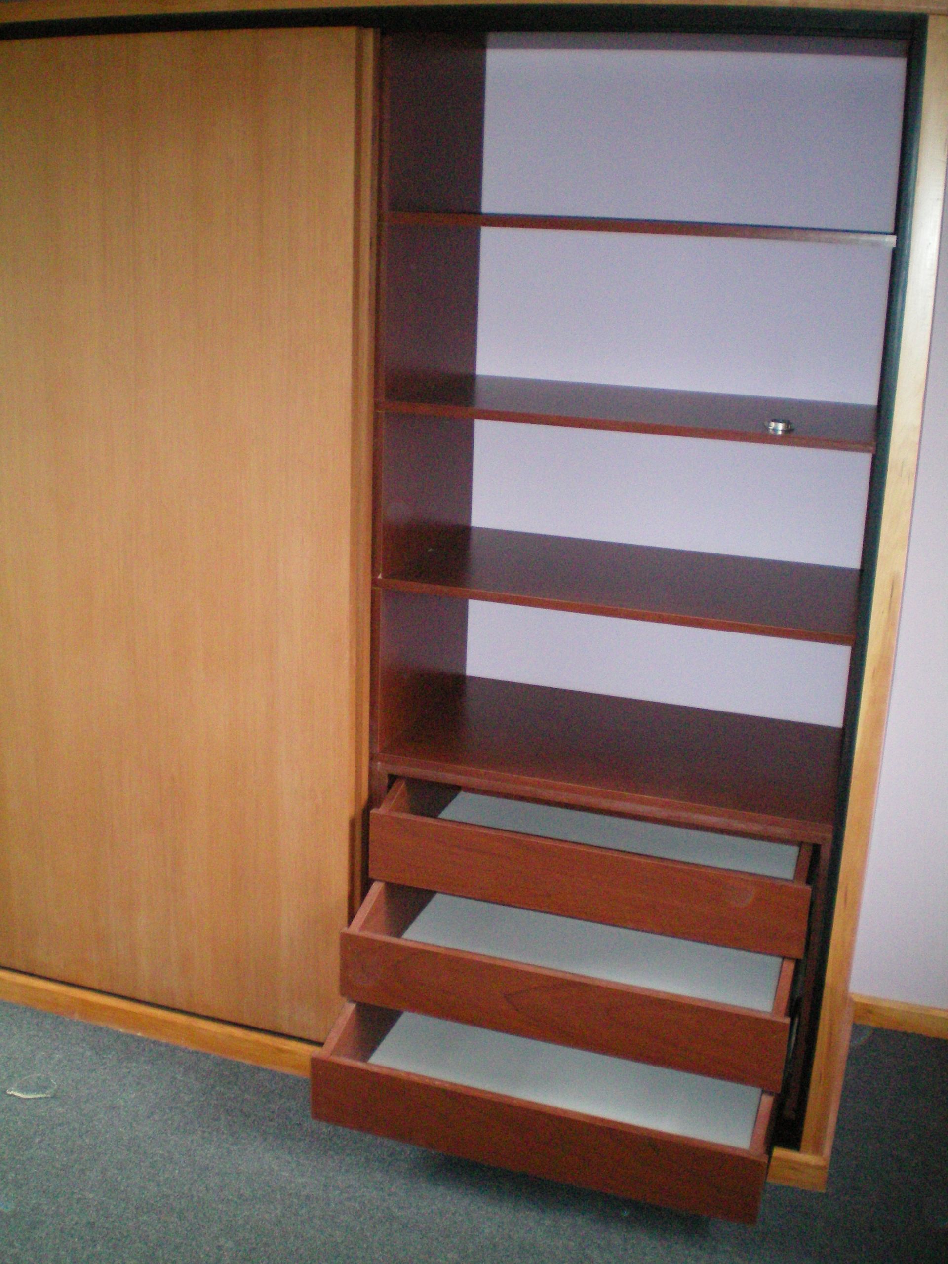 Armario de madera con estantes abiertos para guardar ropa doblada y cajas de almacenamiento, además de tres cajones en la parte inferior.