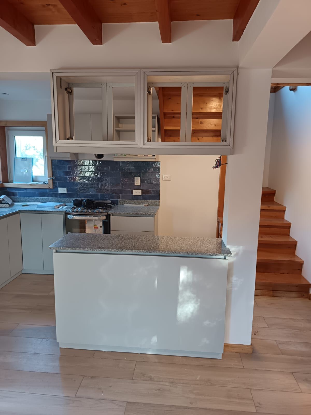 Cocina pequeña con gabinetes blancos, salpicadero de azulejos azules, isla, vigas de madera en el techo