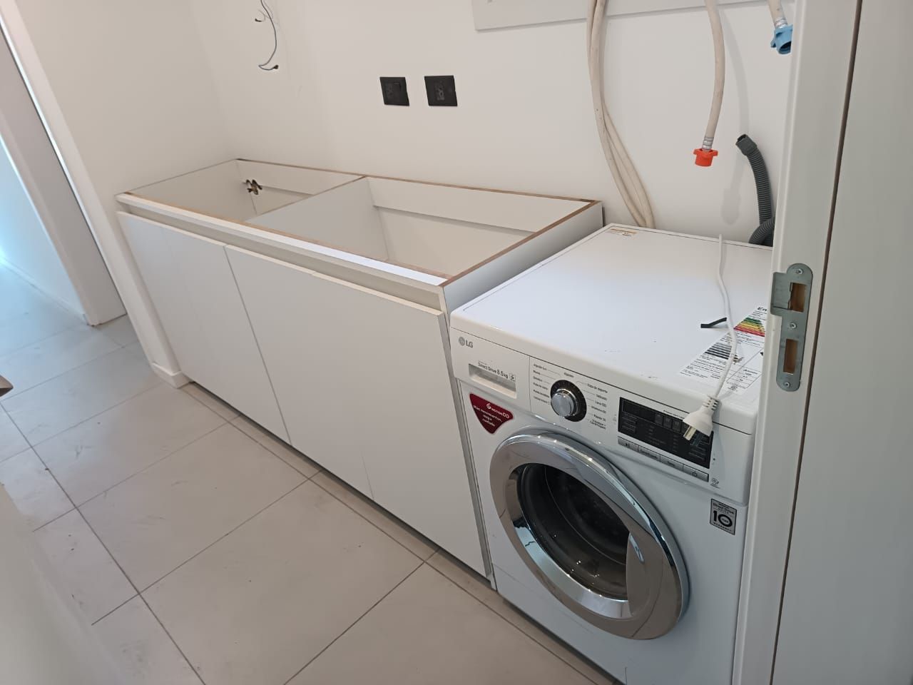 Muebles de cocina blancos con cajones extraíbles y una despensa alta con estantes de rejilla, instalados sobre un suelo de baldosas.