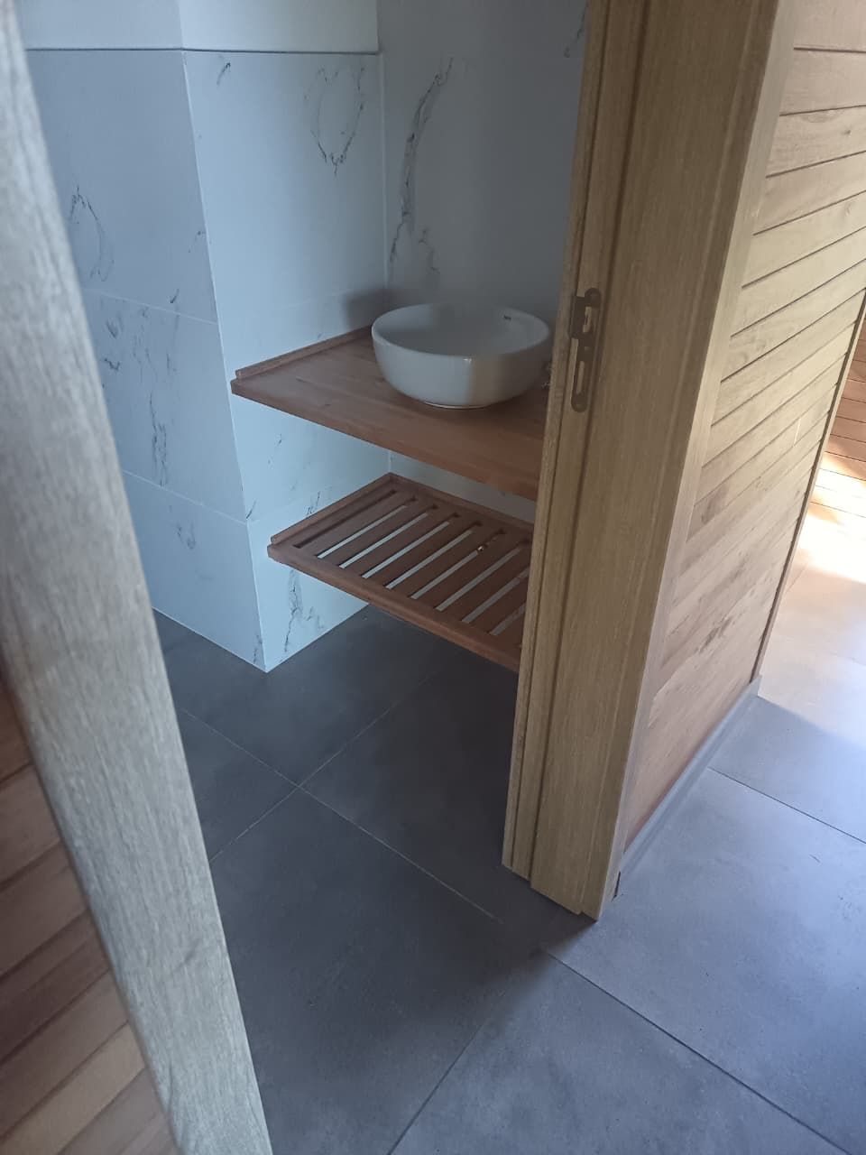 Panel de pared de madera de tonos claros con un televisor de pantalla plana montado y un mueble flotante debajo, en un interior moderno.