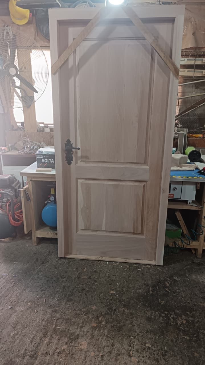 Marco de puerta de madera sin acabado con puerta de dos paneles, ubicado en un taller.