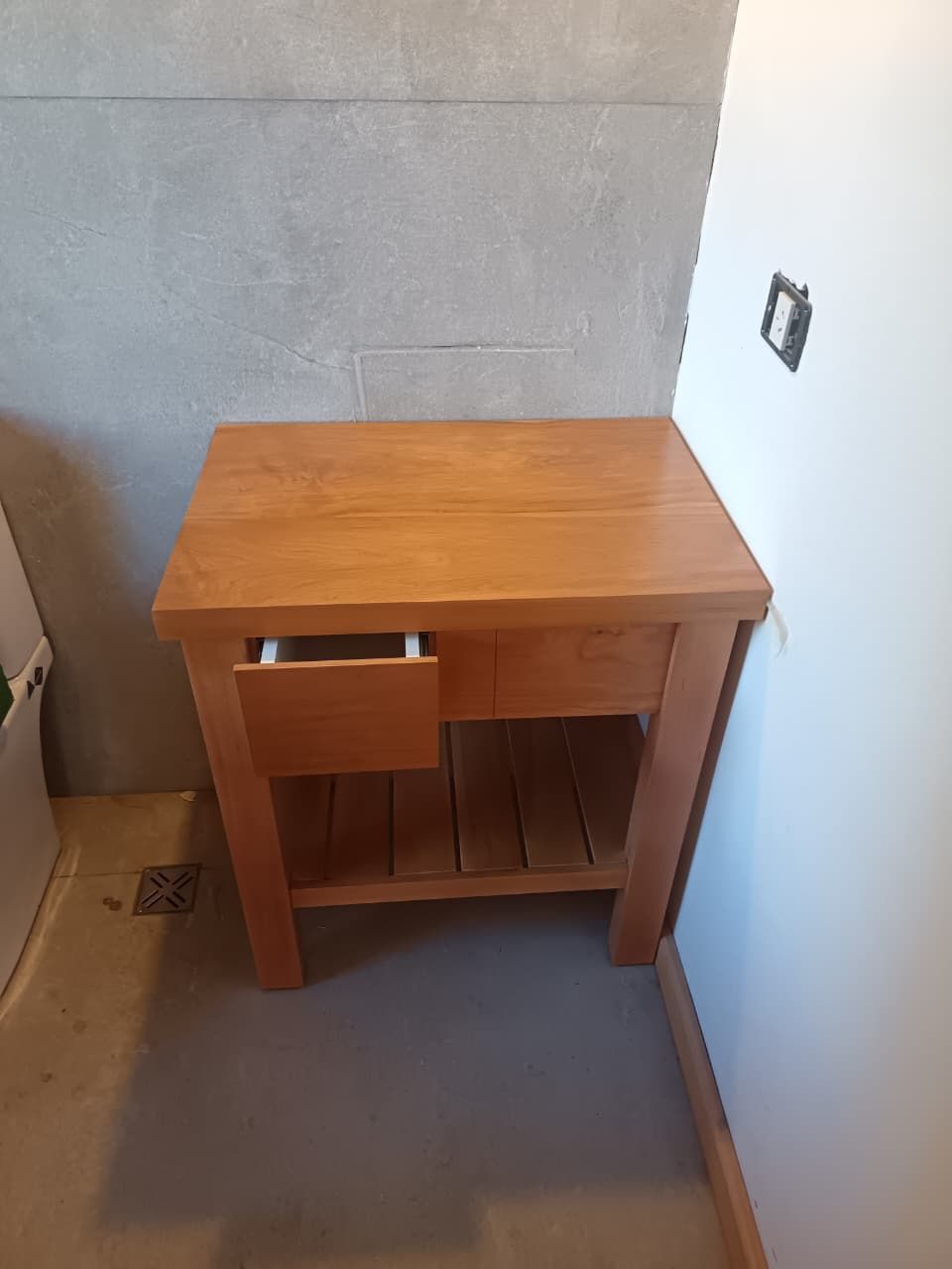 Pequeño escritorio de madera con silla incorporada en una esquina contra una pared blanca y gris.