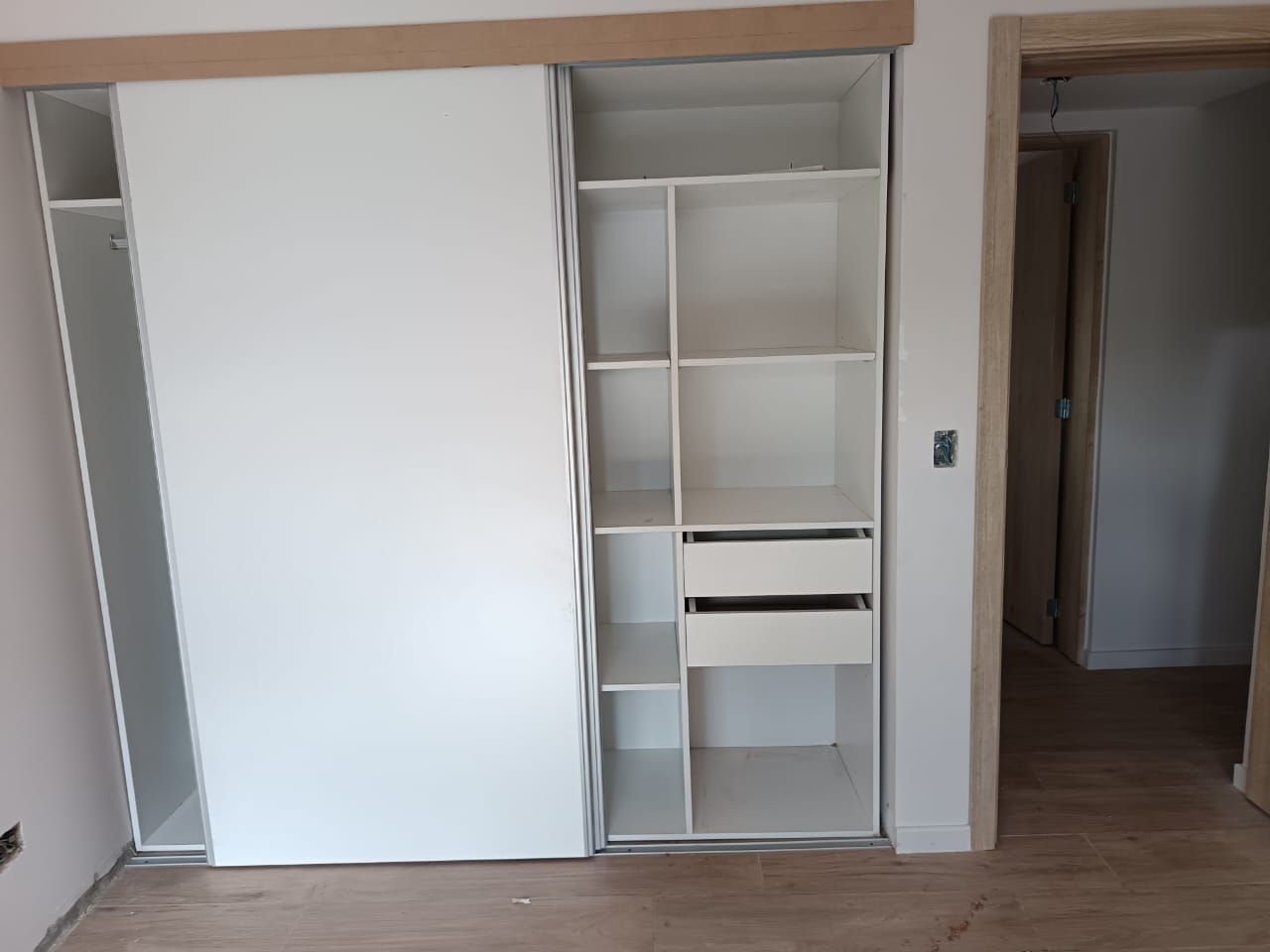 Armario empotrado con puertas correderas blancas y estantes abiertos en una habitación minimalista.