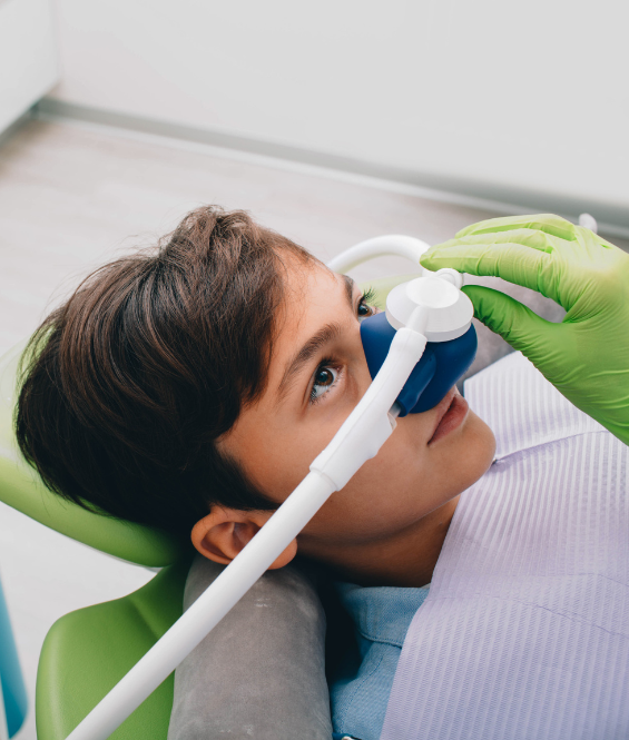 A young boy is laying in a dental chair with an oxygen mask on his face