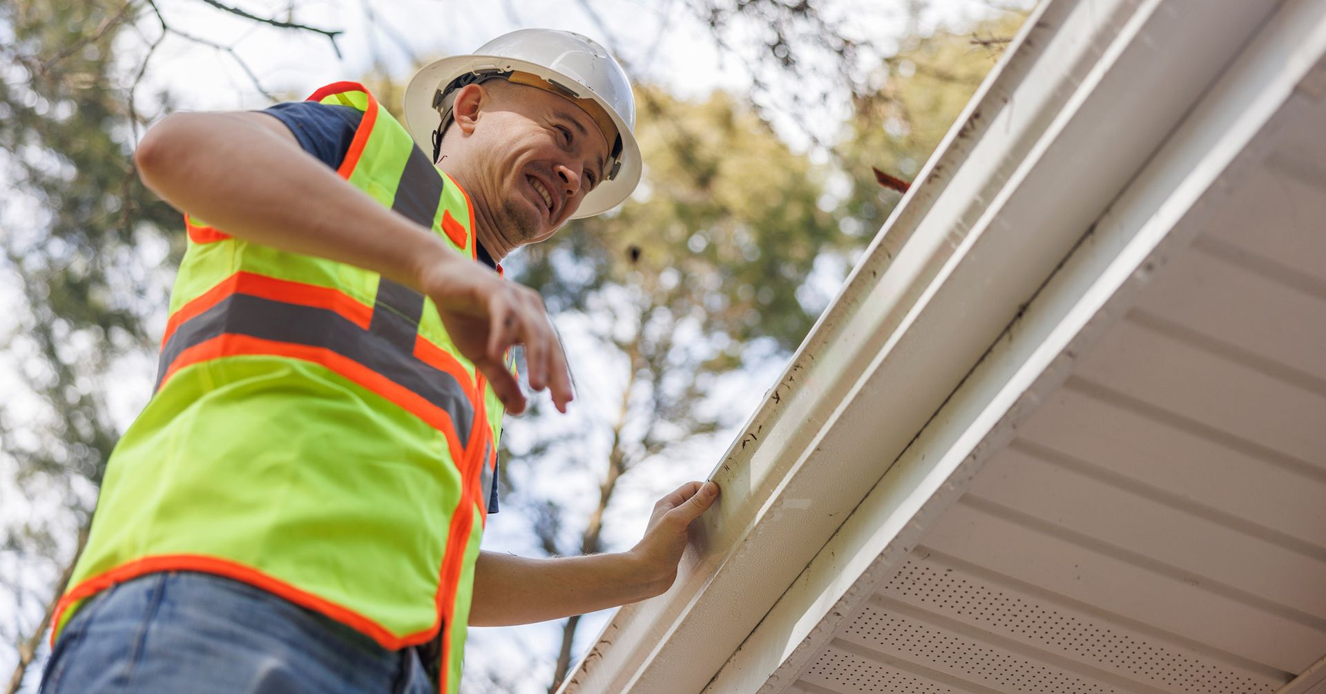 A man in a hard hat and safety vest stands beside a house, representing Art's Custom Seamless Gutter