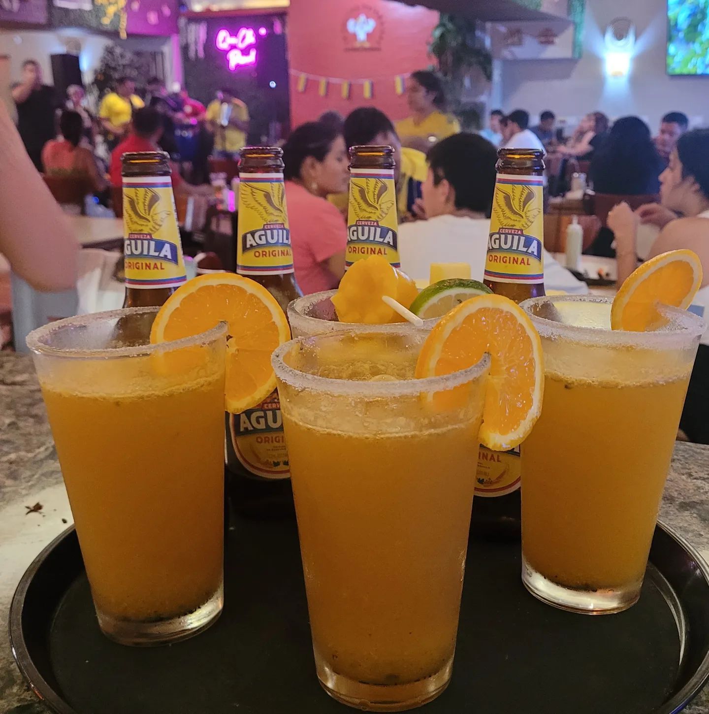 A tray of drinks with a bottle of aguila beer in the background