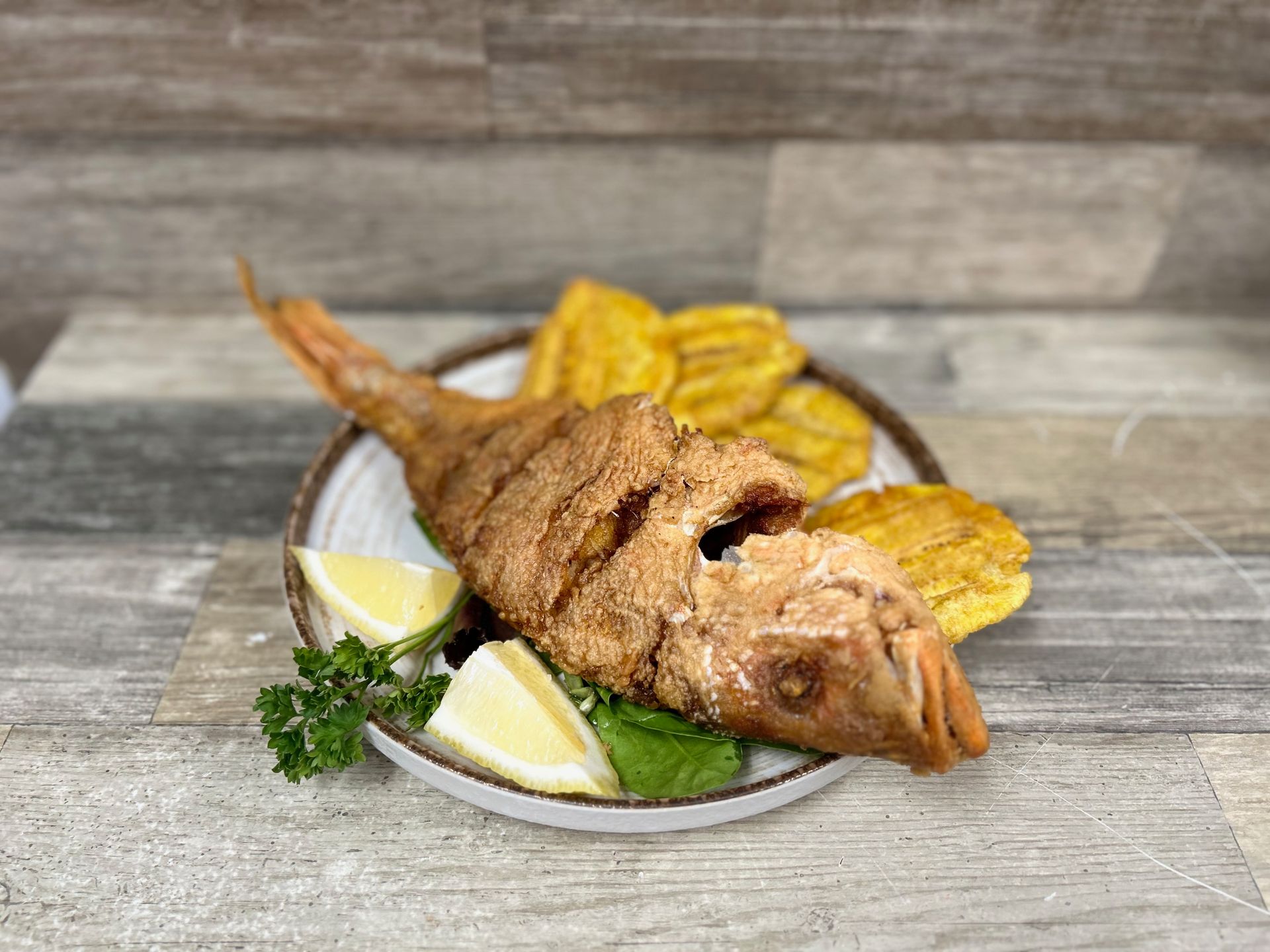 A fried fish on a plate with plantains and lemon slices.