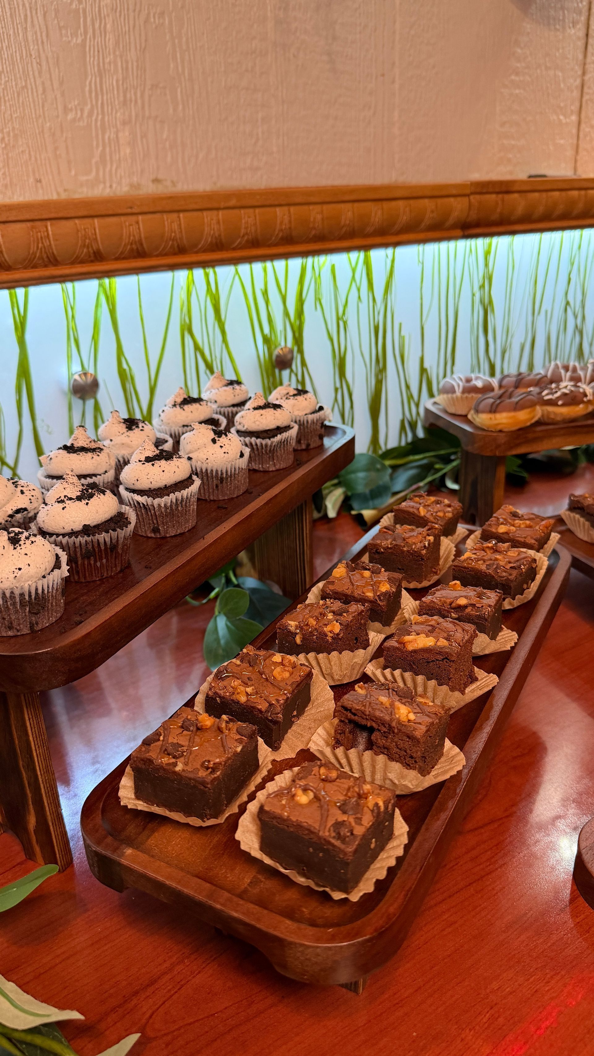 Dessert display: brownies and cupcakes on wooden trays. Greenery in the background.