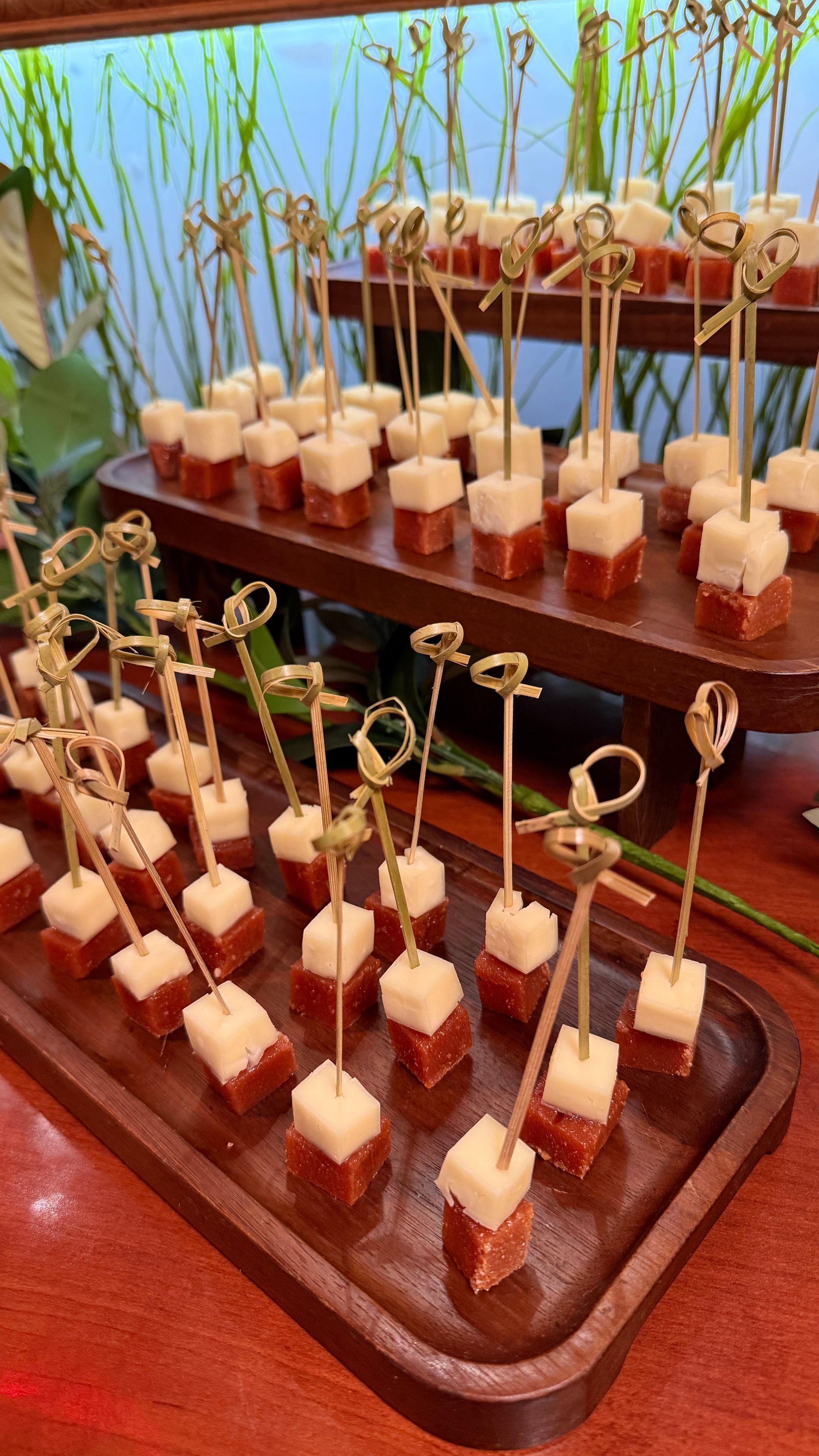 Appetizer skewers: cheese cubes atop reddish squares, arranged on wooden trays.