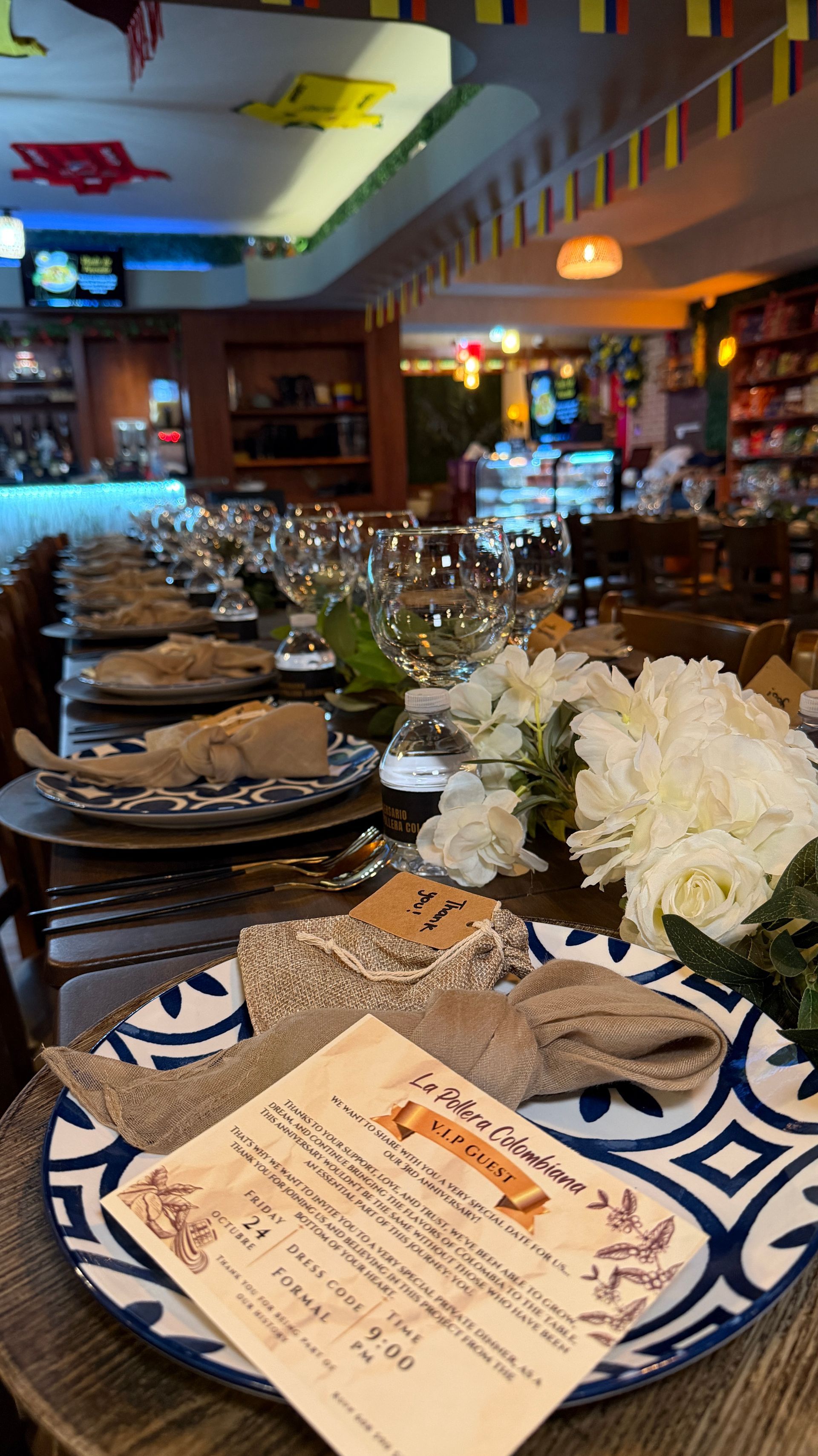 Long dining table set for a meal in a restaurant with floral centerpiece and blue and white plates.