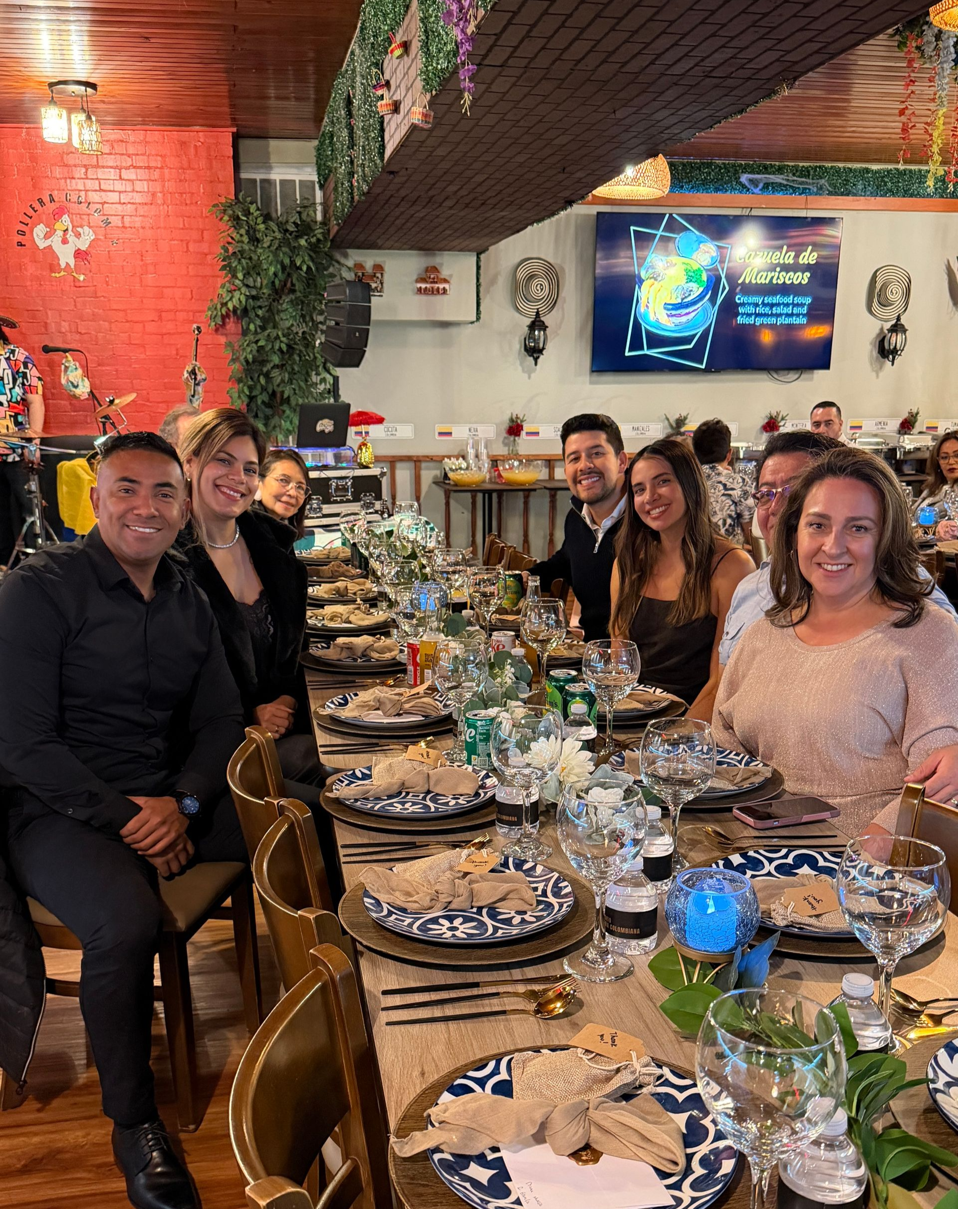 People seated at a long table, set with plates and glasses, in a restaurant.