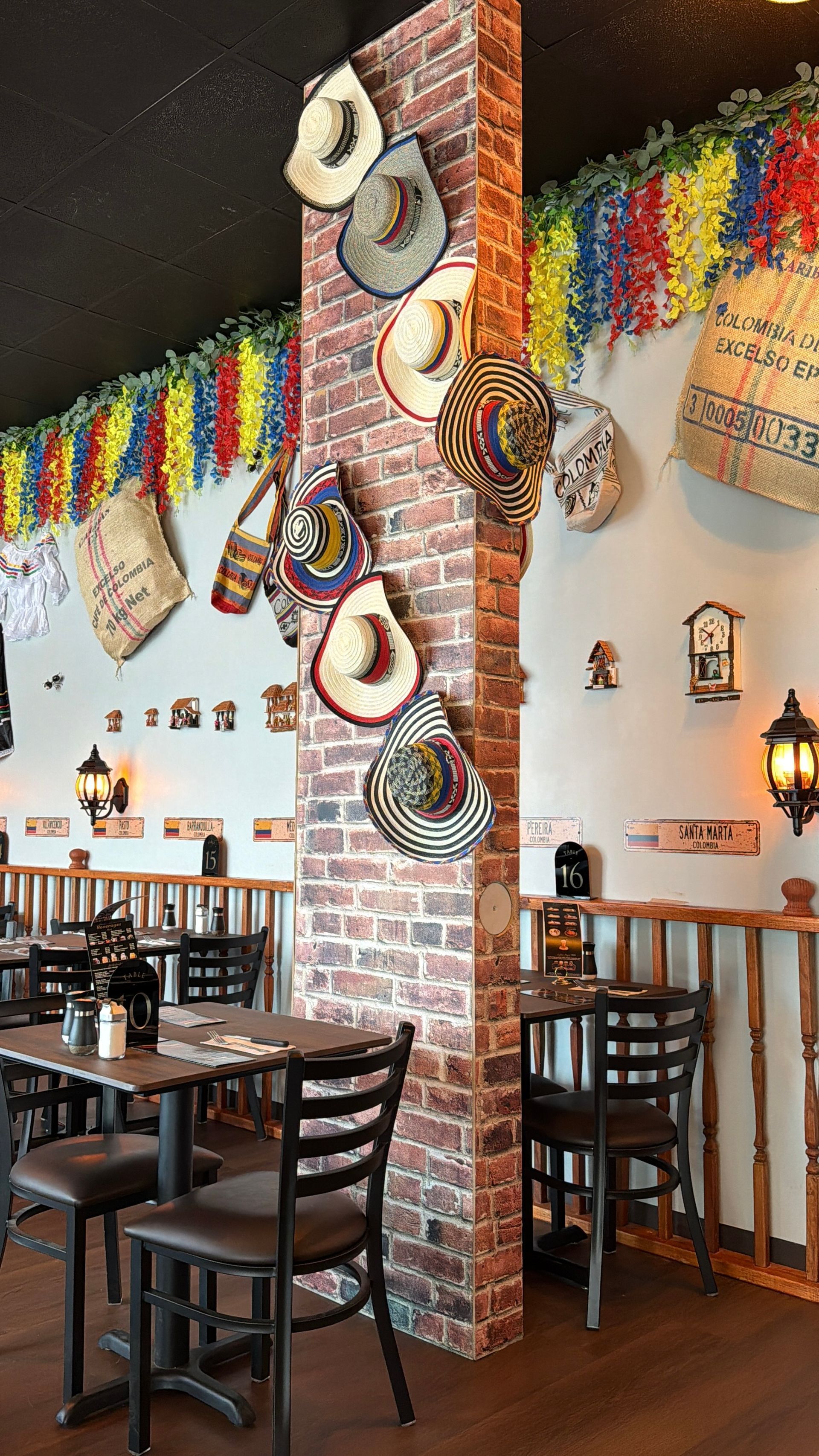 Restaurant interior with tables, chairs, and brick pillar decorated with sombreros. Colorful garland hangs overhead.