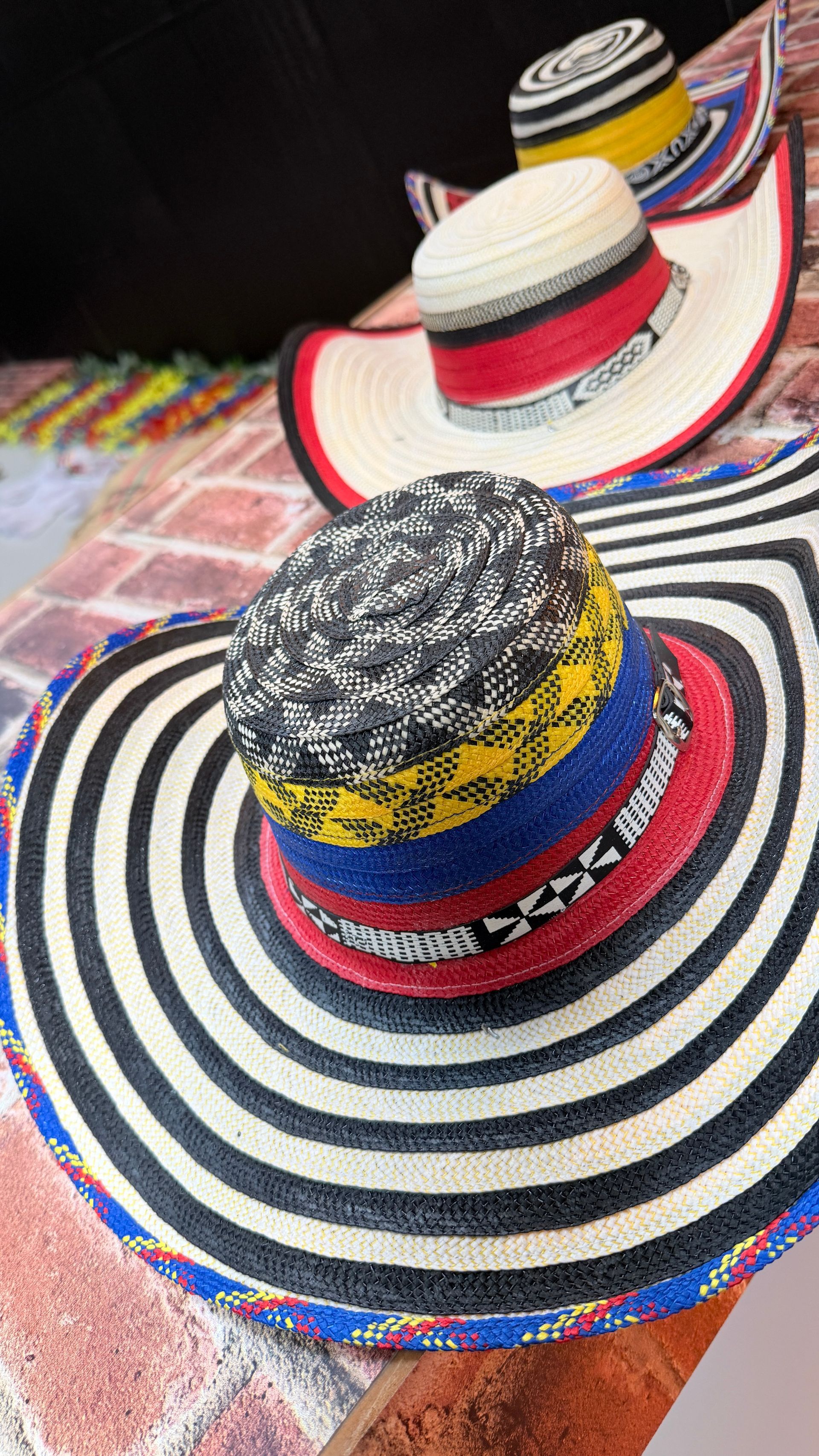 Three Colombian Vueltiao hats with striped brims, colorful bands, and varied crowns, displayed on bricks.