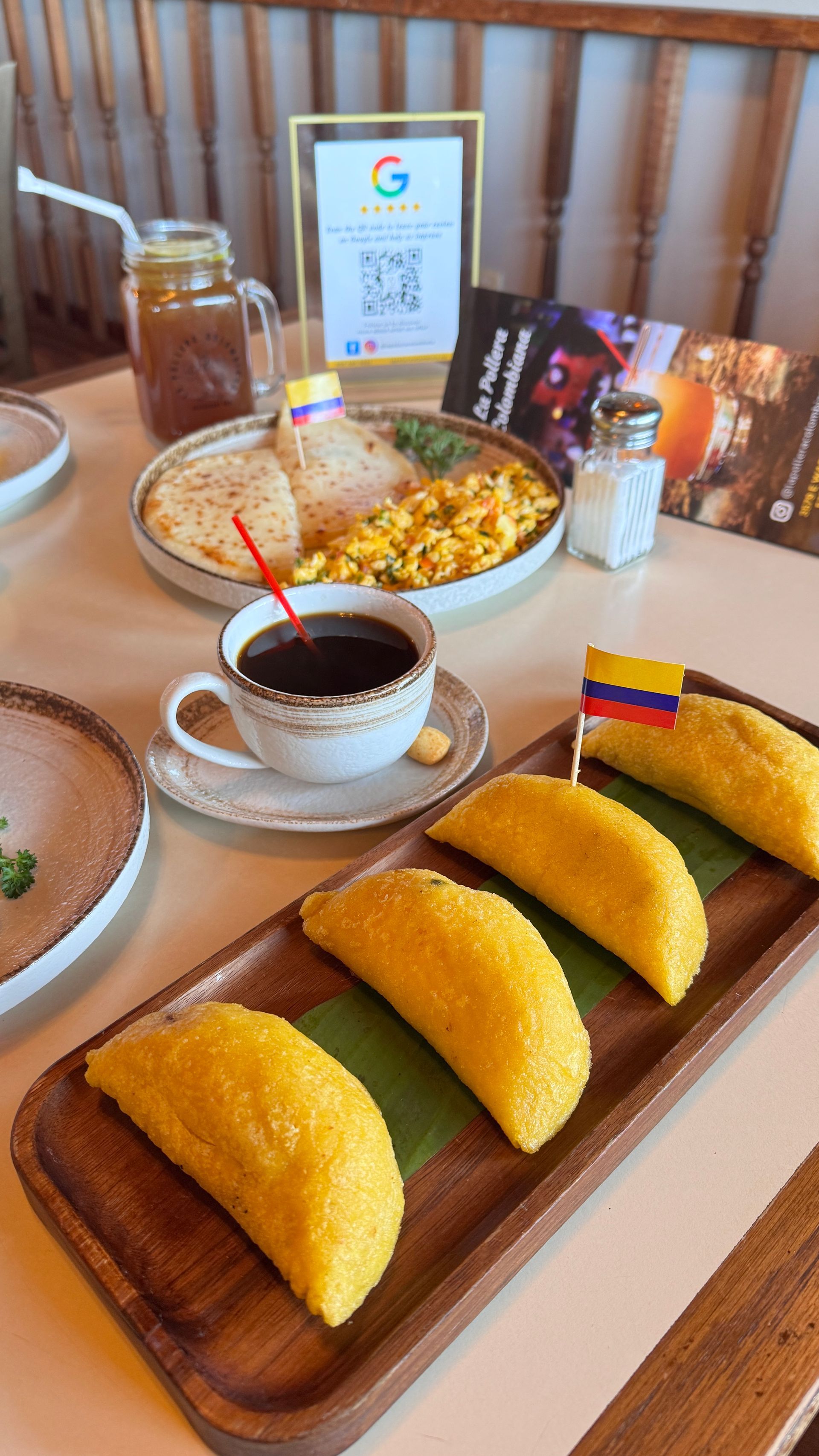 Table with Colombian breakfast: empanadas, scrambled eggs, arepas, coffee, and iced drink.
