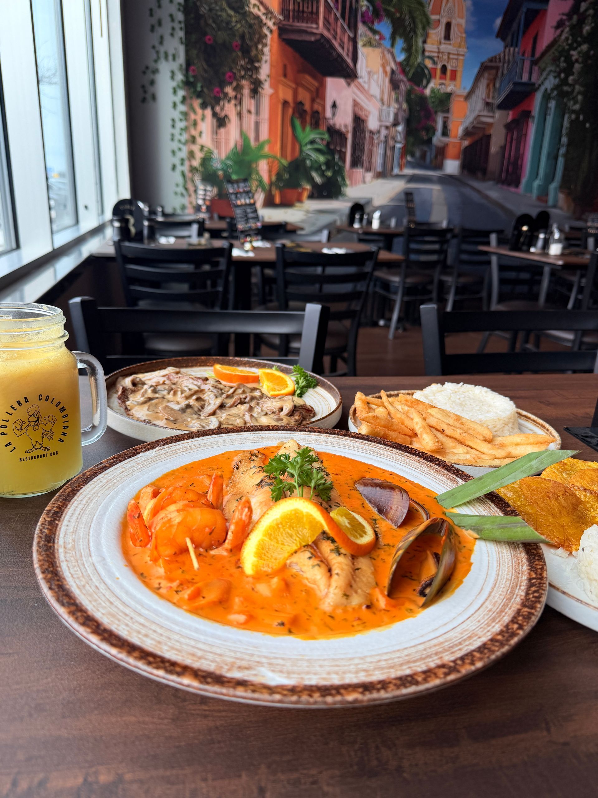 Restaurant table with plates of food, drinks, and a colorful mural.