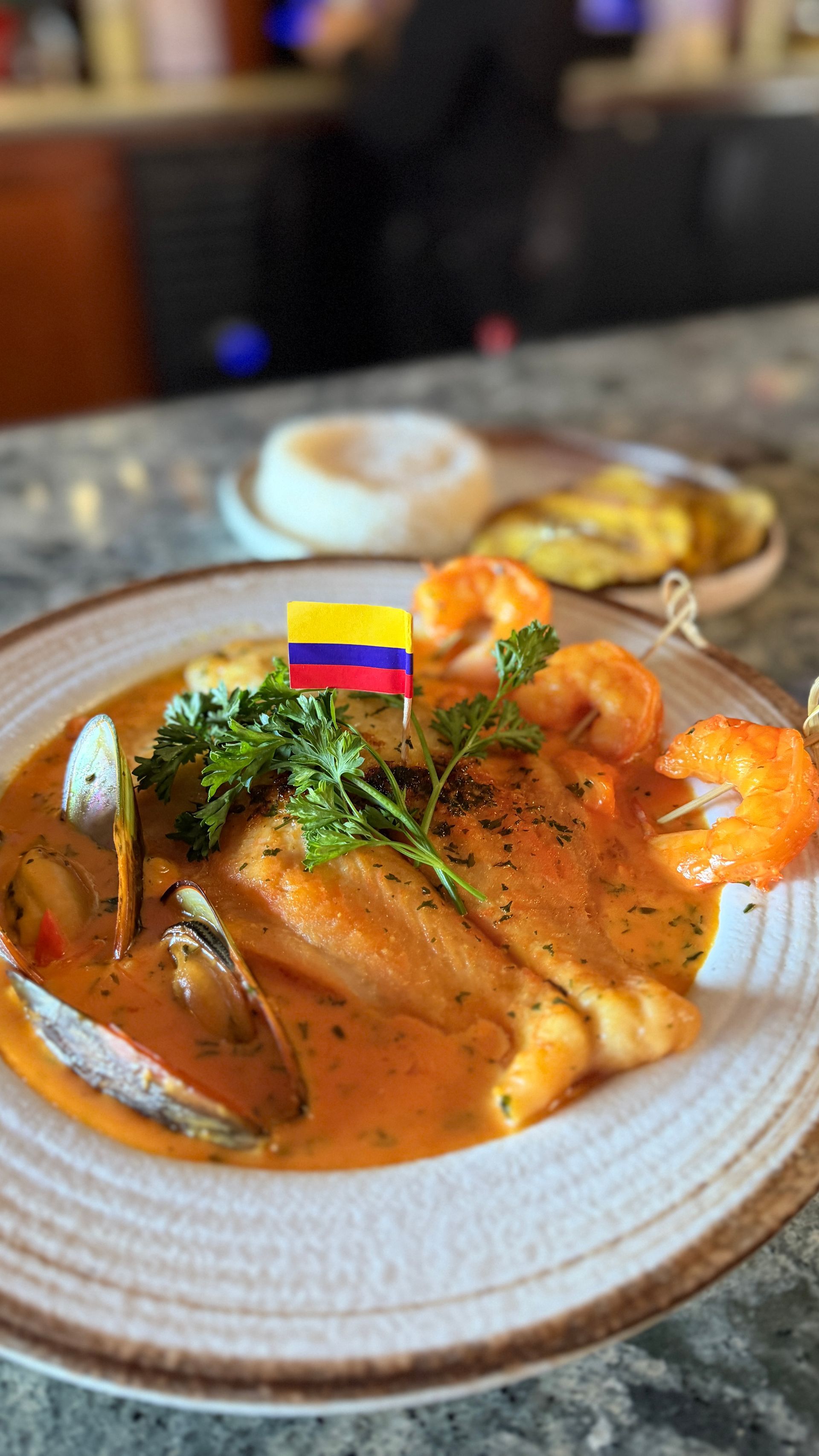 Plate of seafood with sauce, shrimp, clams, and Colombian flag.