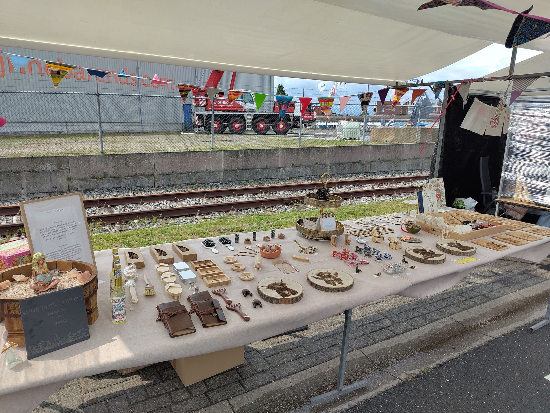 Een knutseltafel met handgemaakte houten voorwerpen, naast spoorrails. Op de achtergrond zijn een kraan en vlaggen te zien.
