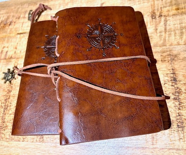 Twee bruine leren notitieboekjes met kompasroosmotief en leren sluitingen.