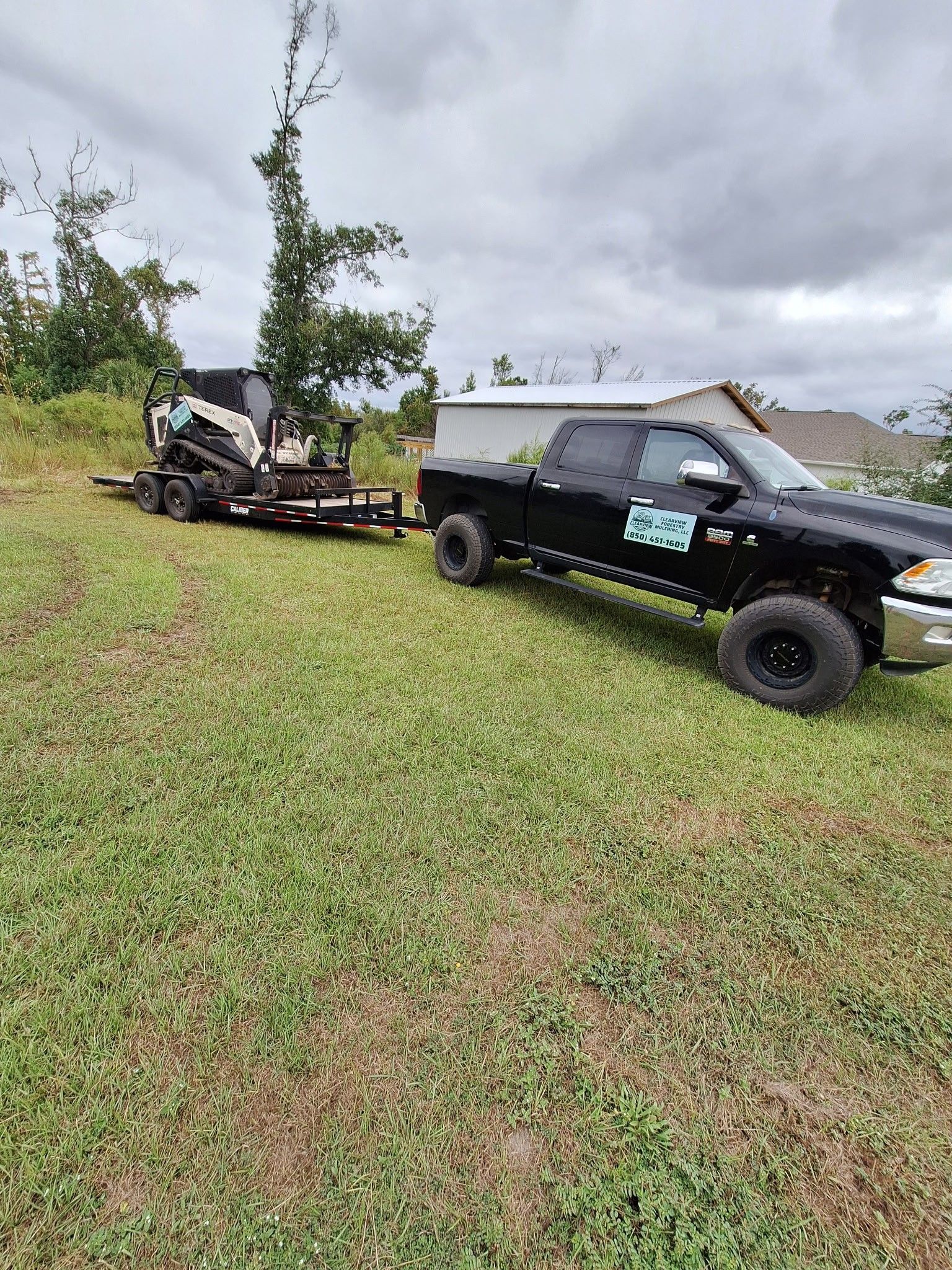 Black truck towing a trailer with landscaping equipment on a grassy hill under a cloudy sky.