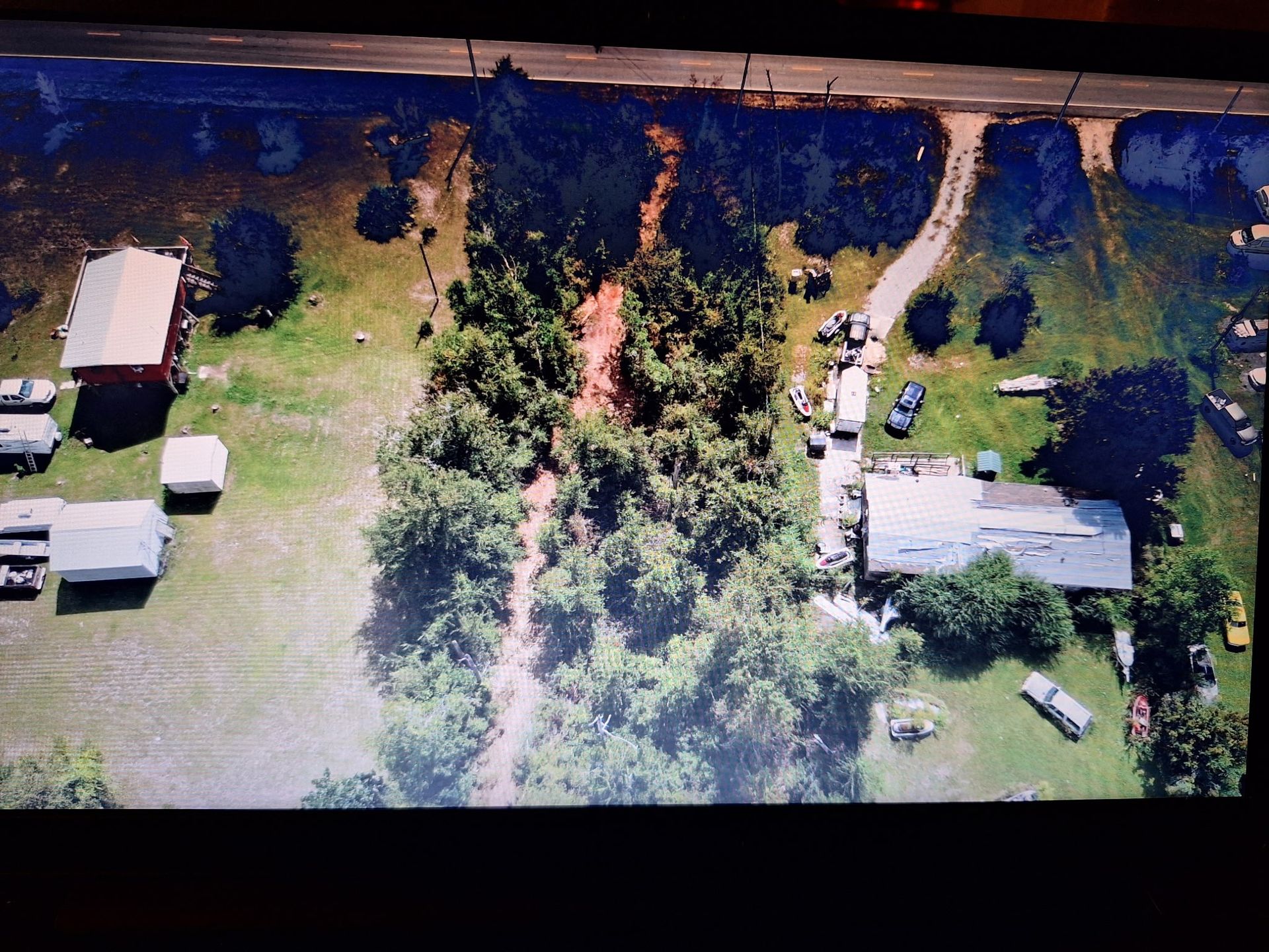 Aerial view of rural properties with trees, houses, vehicles, and a road.