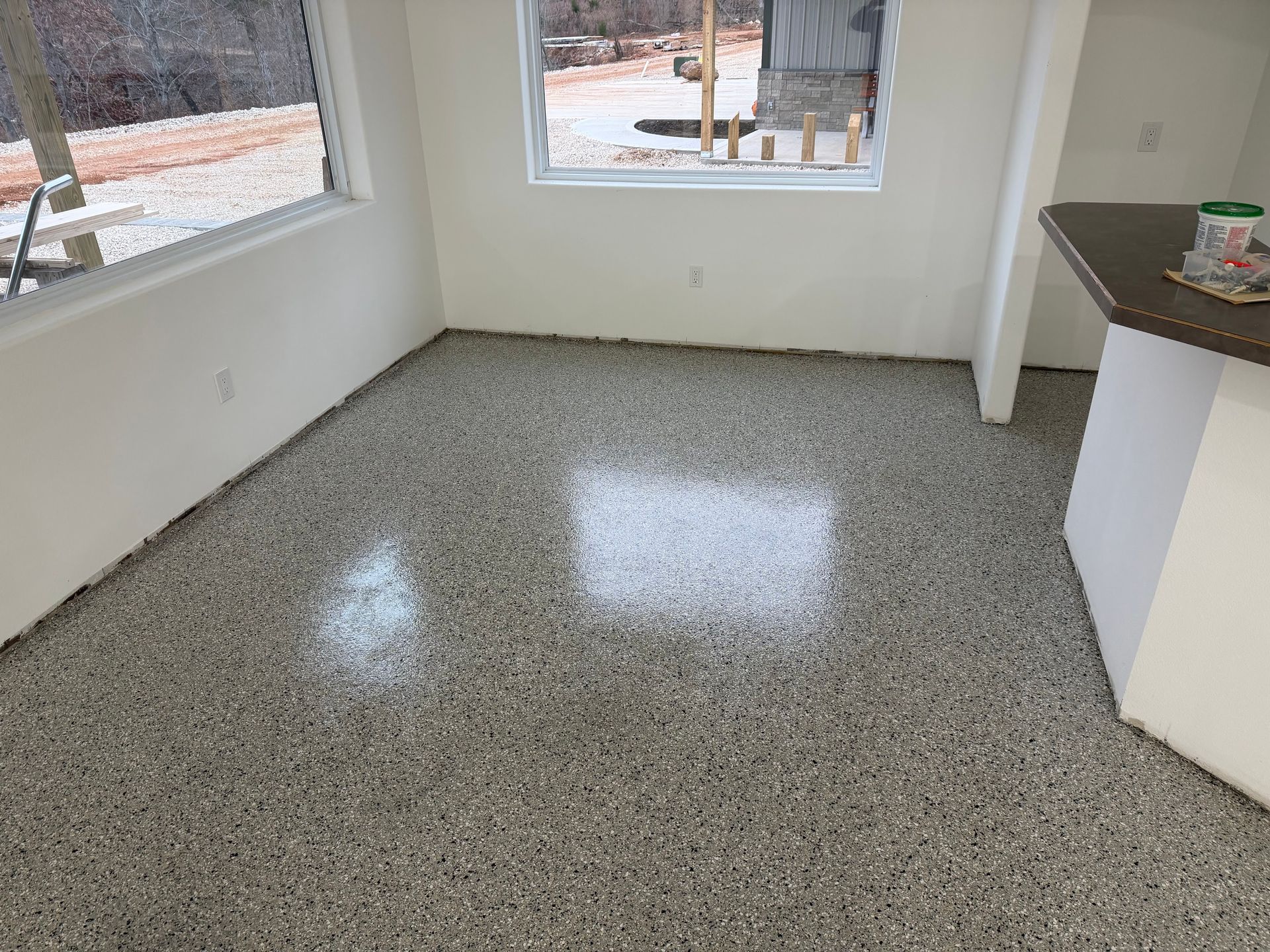 Empty speckled floor in a bright room with large windows and white walls