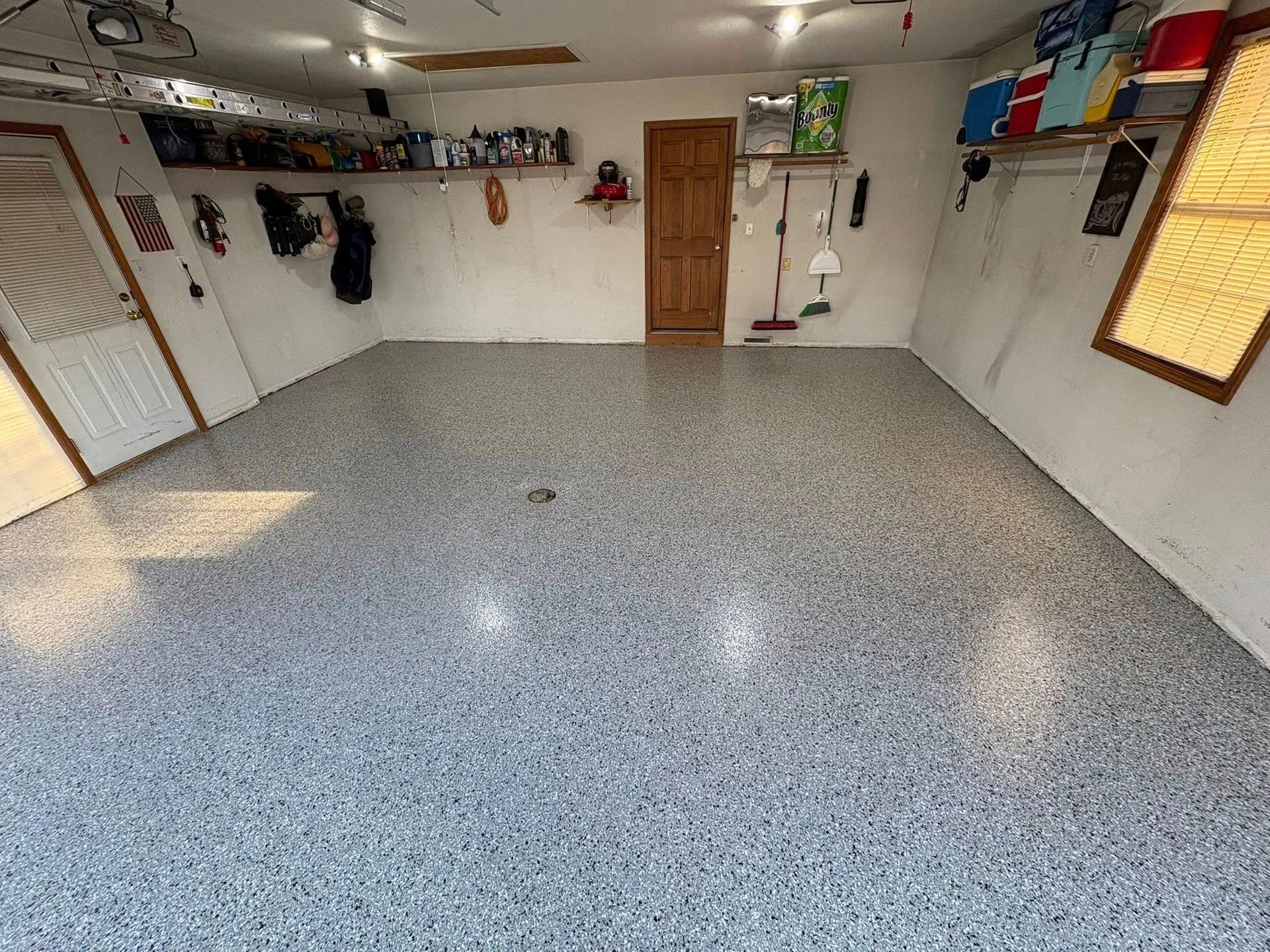 Empty garage with white walls, gray speckled floor, wooden door, and hanging storage shelves.