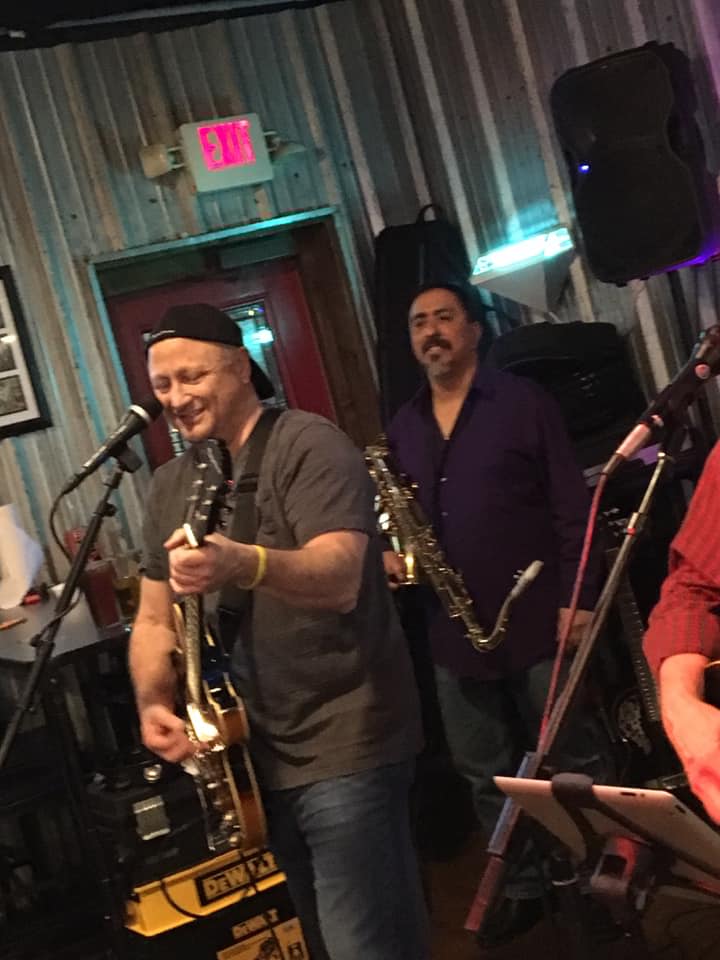 A man is playing a guitar and a man is playing a saxophone.