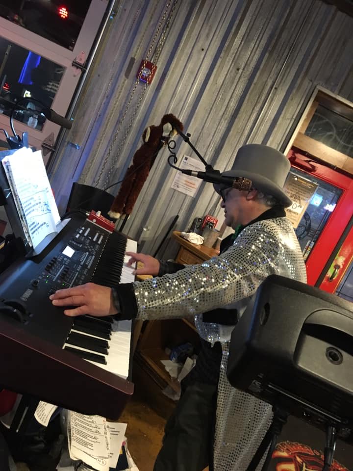 A man in a hat is playing a keyboard and singing into a microphone.