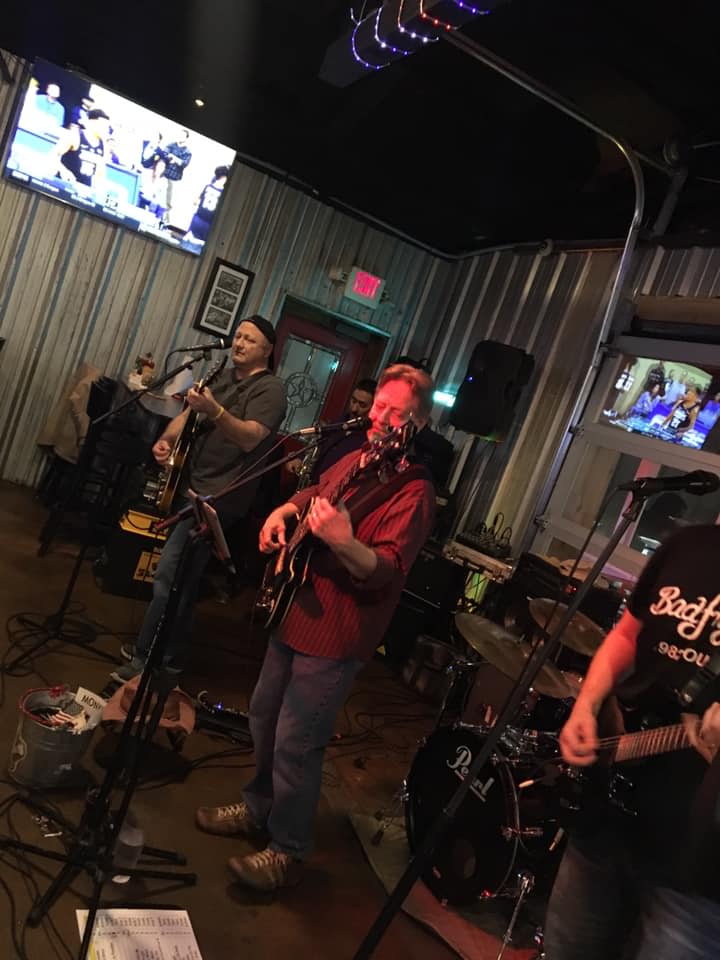 A man is singing into a microphone while playing a guitar in a band.