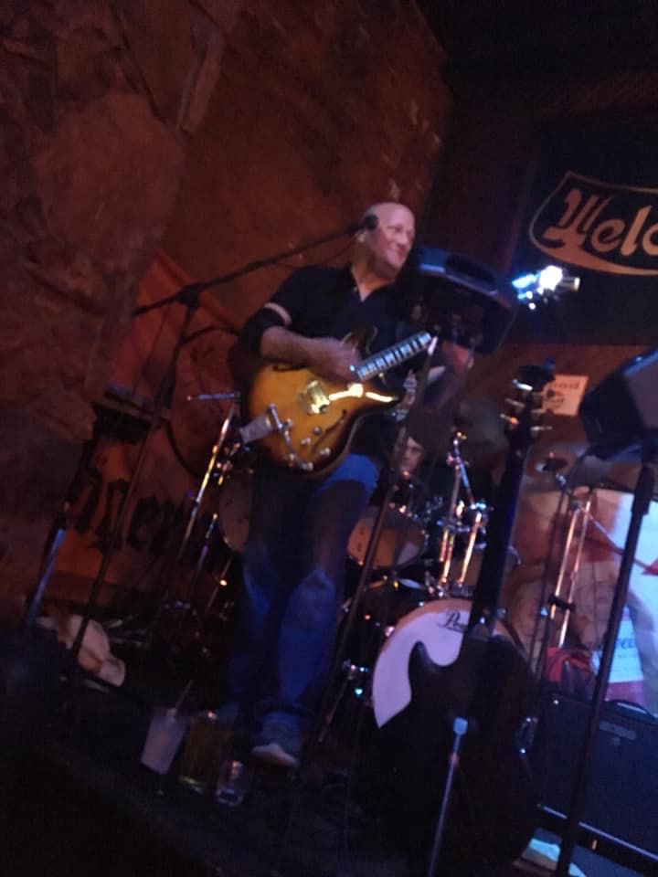 A man playing a guitar in front of a welcome sign