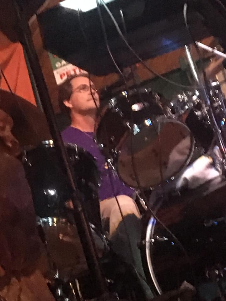 A man in a purple shirt is playing drums