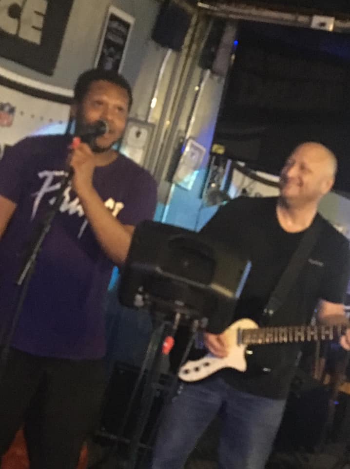 A man singing into a microphone while another man plays a guitar