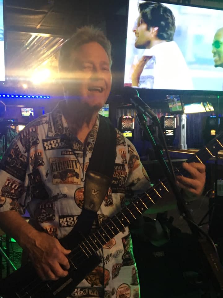A man in a hawaiian shirt is playing a guitar in front of a microphone.
