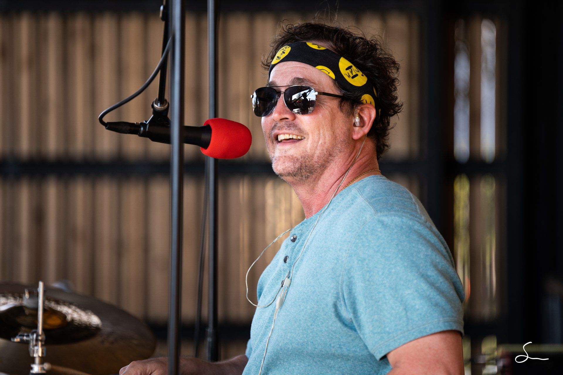 A man wearing sunglasses and a headband is singing into a microphone.