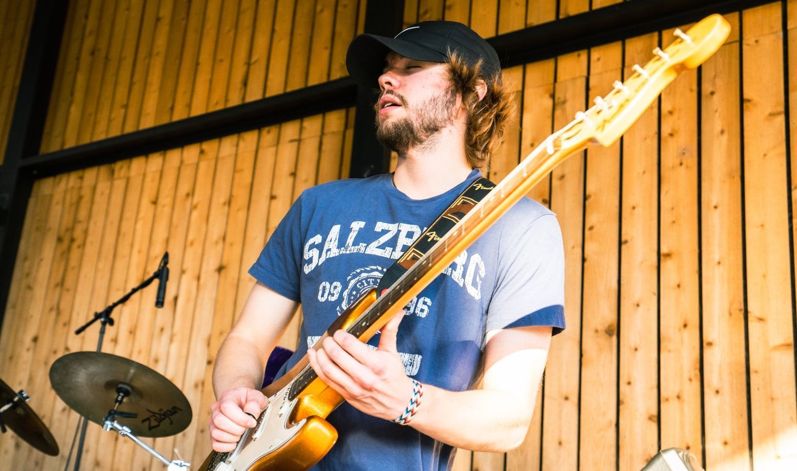 A man is playing a guitar in front of a wooden wall.