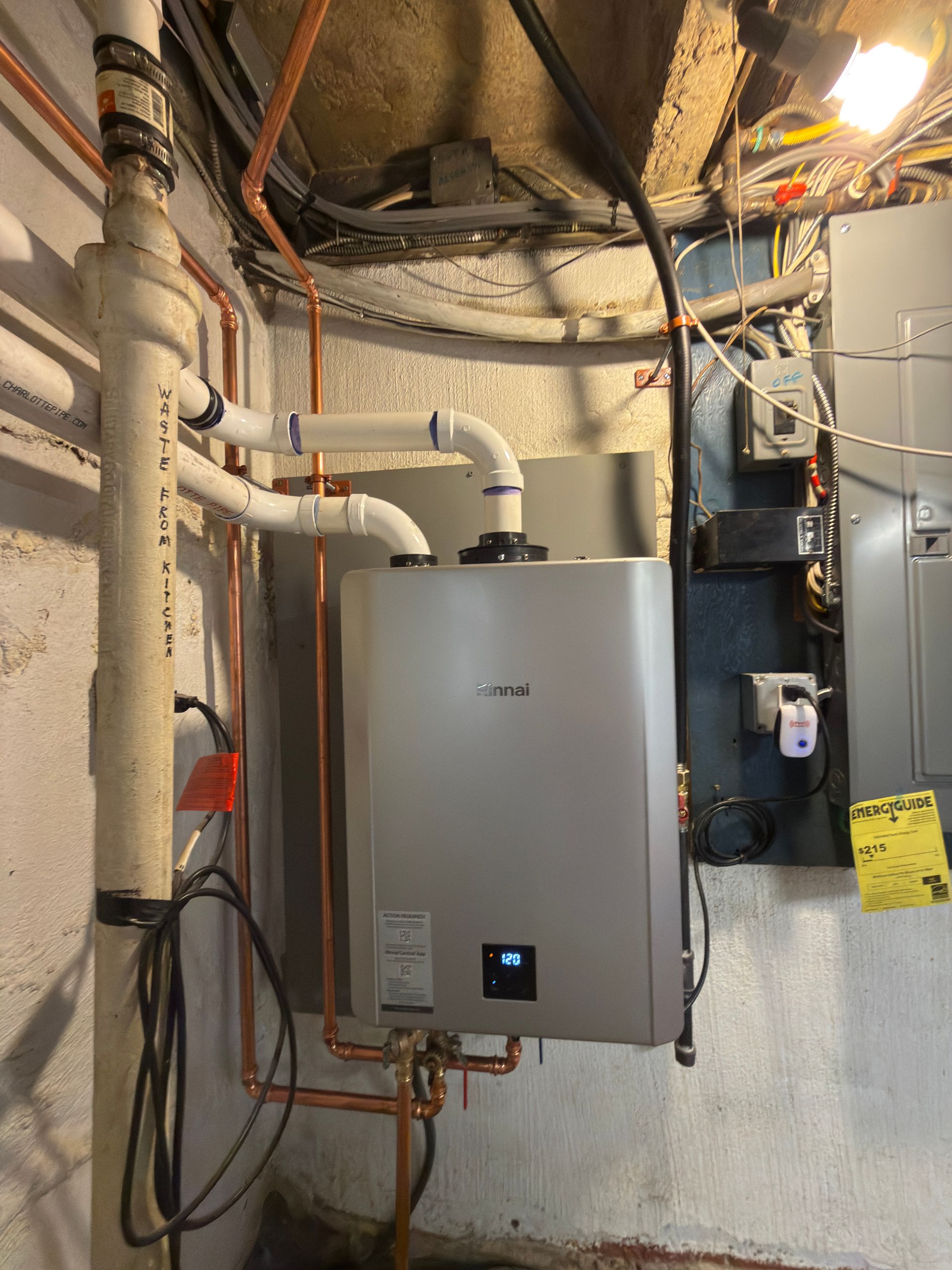 A wall-mounted water heater with copper pipes and white PVC venting in a basement.
