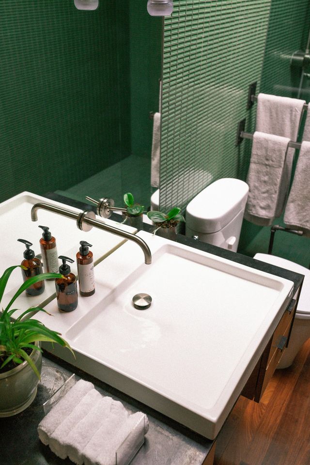Modern bathroom with a white sink, green tiled walls, and towels.
