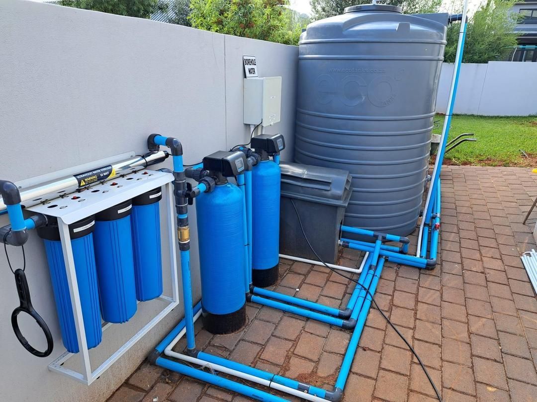 A water filter system is sitting on a brick patio next to a water tank.