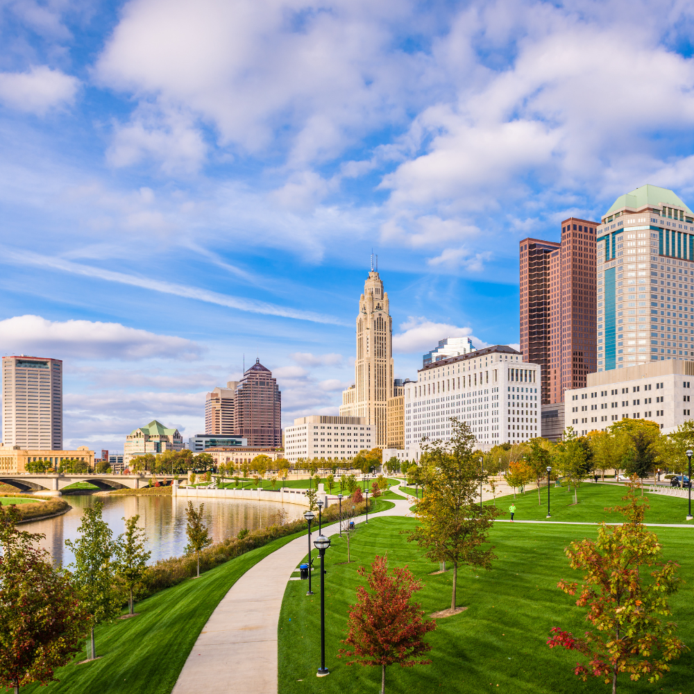 A city skyline with a park in the foreground and a river in the background.