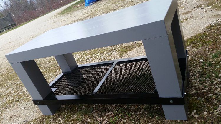 A gray and black table is sitting on top of a dirt field.