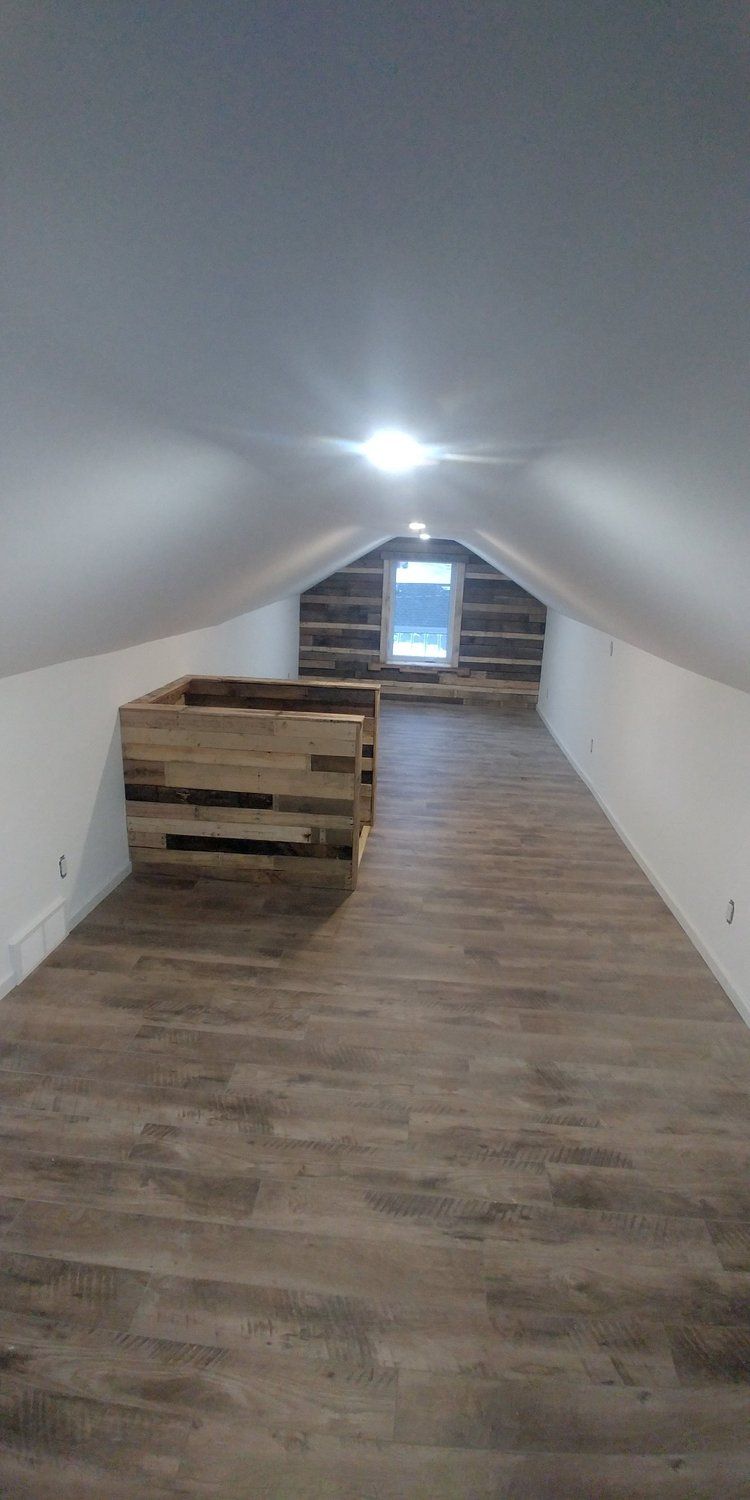 An empty attic with a wooden floor and a window.
