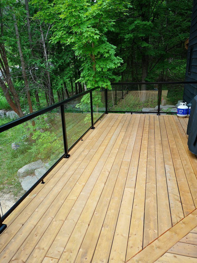 A wooden deck with a glass railing and trees in the background.